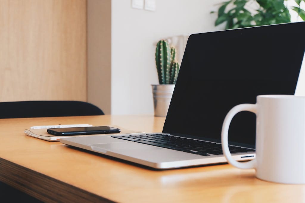A tidy office desk with a laptop, coffee mug, and smartphone in a well-lit workspace.