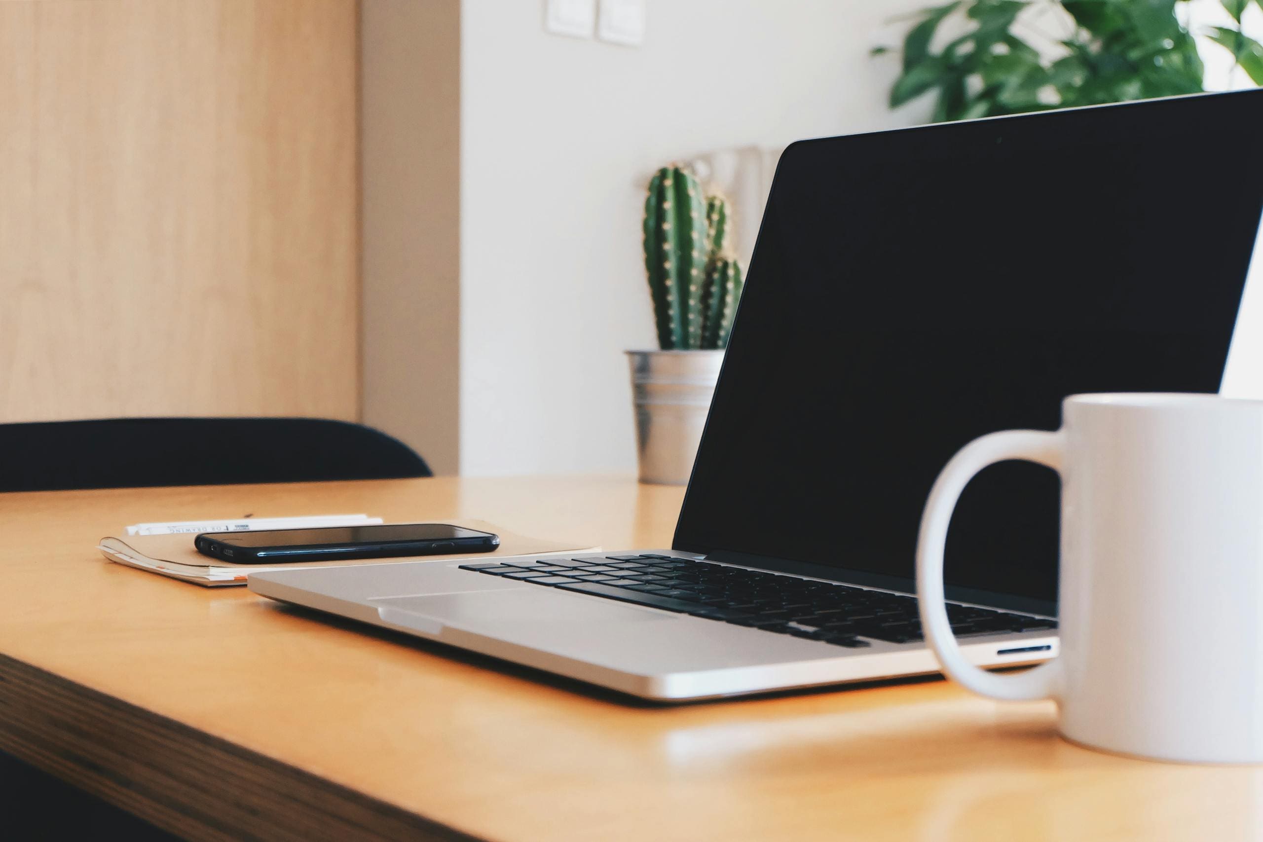 A tidy office desk with a laptop, coffee mug, and smartphone in a well-lit workspace.