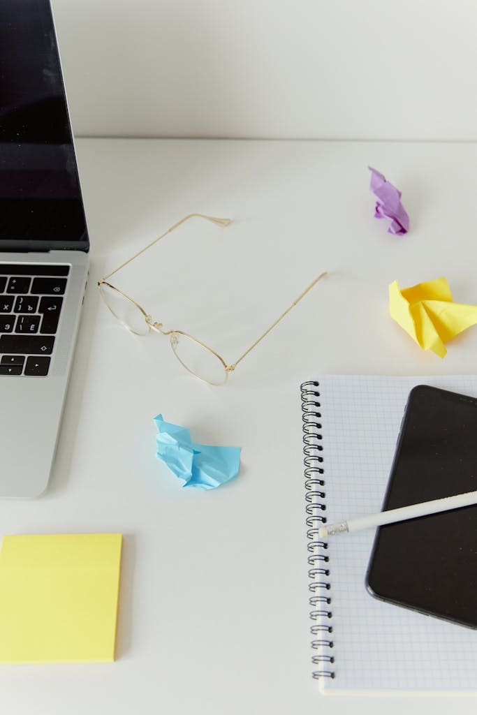 Modern workspace featuring a laptop, notepad, and crumpled colorful papers on a desk.